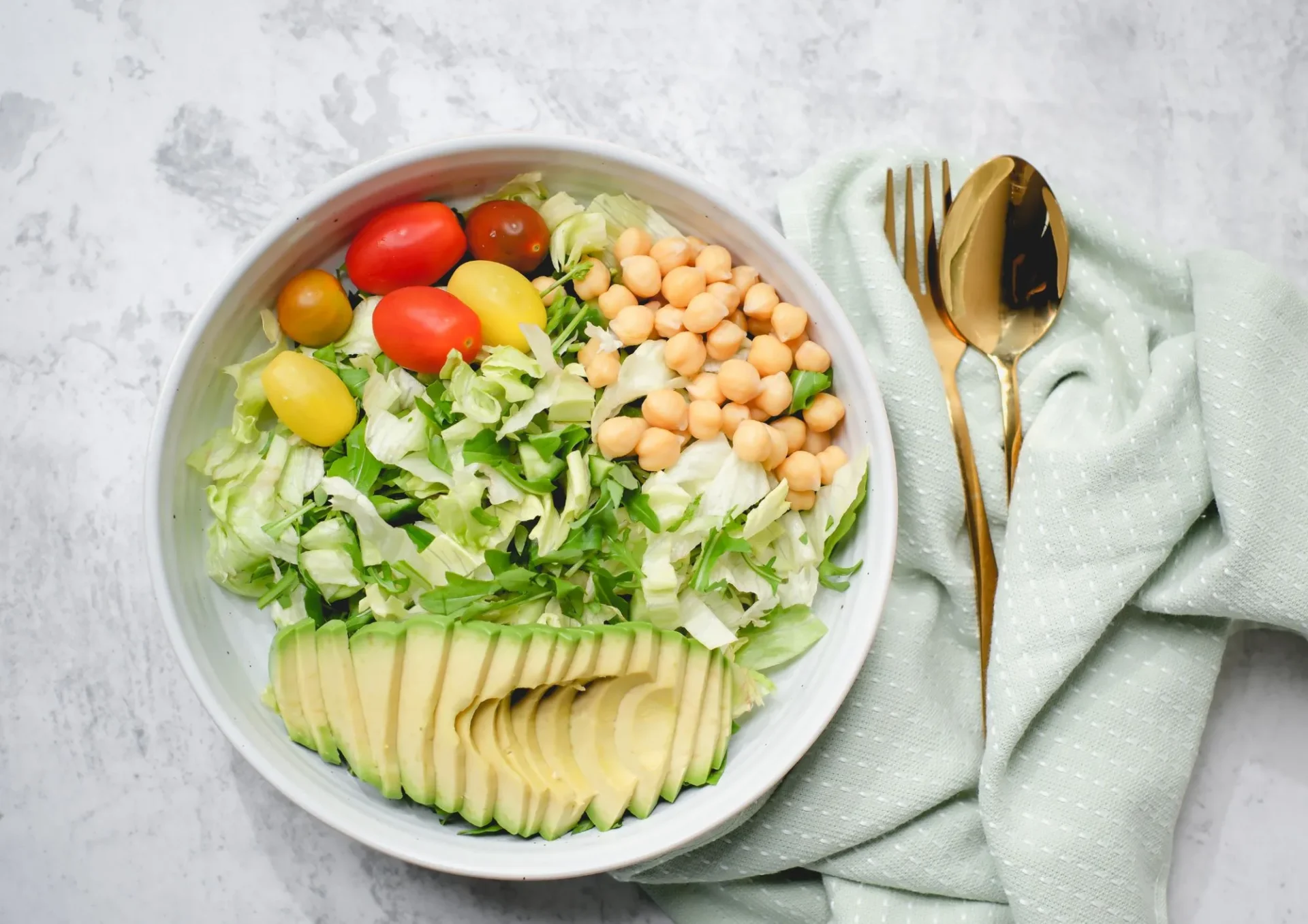 assiette équilibrée composé de pois chiche, d'avocat et de salade, avec une cuillère à soupe et une fourchette.